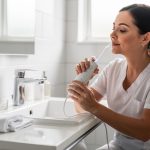 Hydropulseur dentaire : quelles sont les contre-indications à connaître Une femme utilise avec prudence un hydropulseur dans une salle de bain lumineuse, ambiance propre et rassurante, éclairage naturel doux.