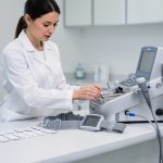 Une médecin prépare un électrocardiographe dans un cabinet médical propre, avec une ceinture ECG et des électrodes soigneusement rangées sur un plan de travail.